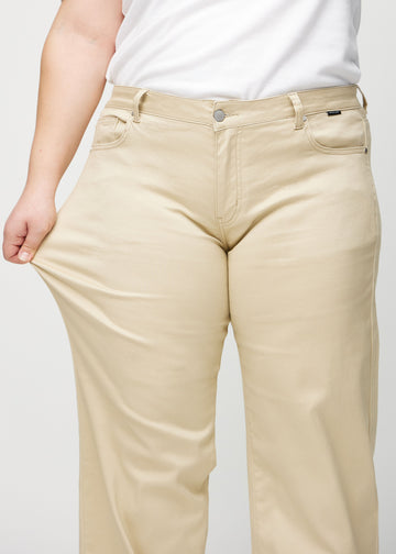 Plus-size model strækker jeansene ved låret for at vise stretch.