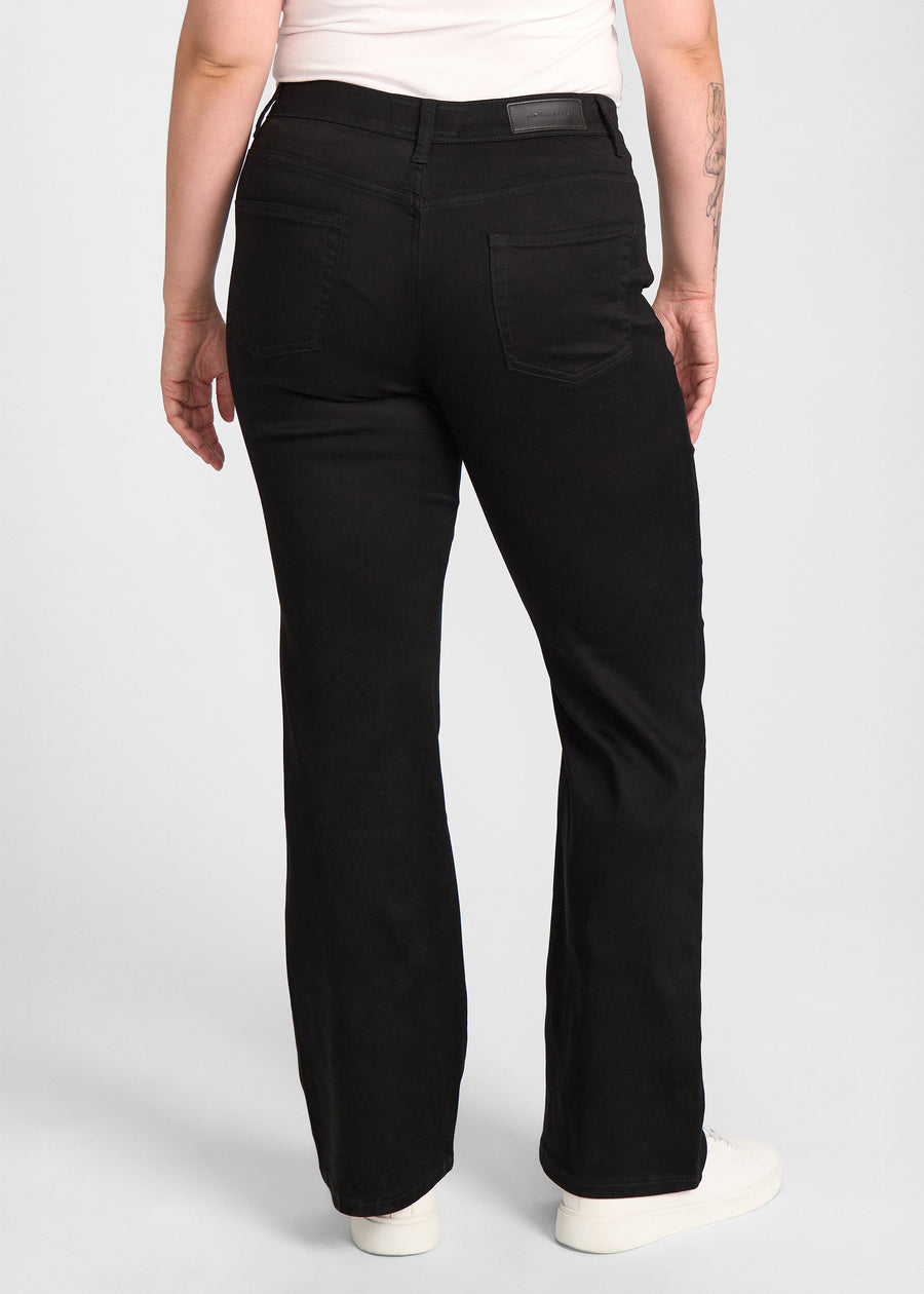 Sort bootcut jeans, modelnavn Ravens, som sidder tæt om hofter og lår med et let svaj fra knæet og ned, set bagfra, så man kan se hele produktet. på en plus-size model.