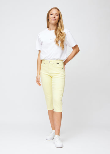 Model træder ind i billedet, strækker i sine lysegule slim capris, viser dem frem ved at dreje rundt, og går derefter ud af billedet igen.