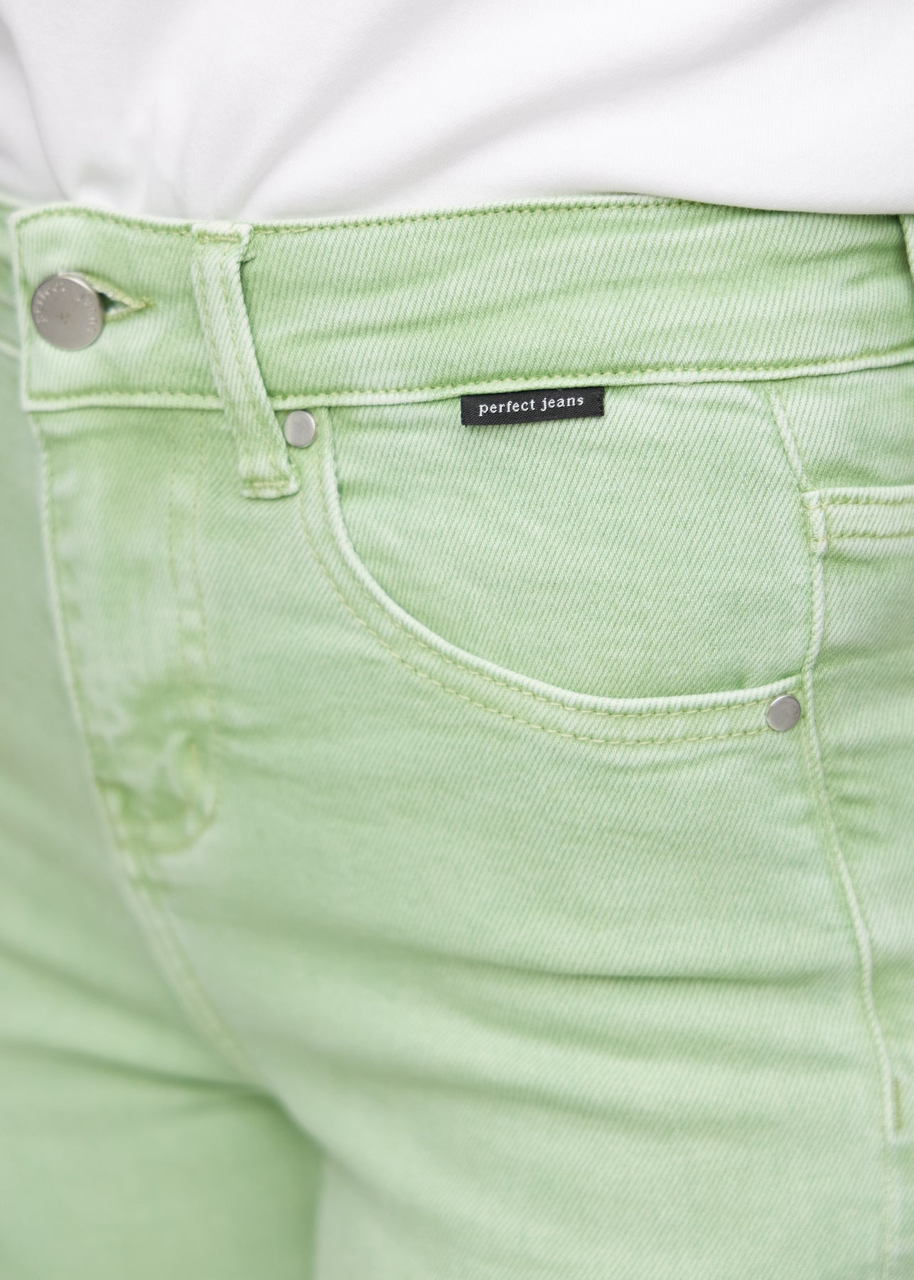 Nærbillede af lysegrønt jeansmateriale med Perfect Jeans logoetiket ved forlommekanten.