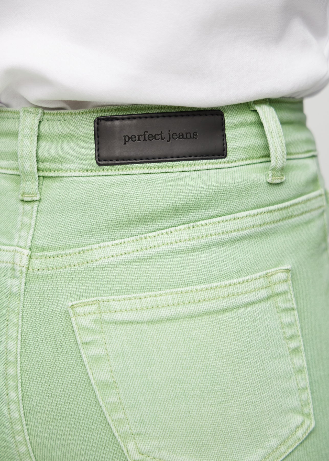 Nærbillede af lysegrønt jeansmateriale med Perfect Jeans læderpatch bagpå i taljen.