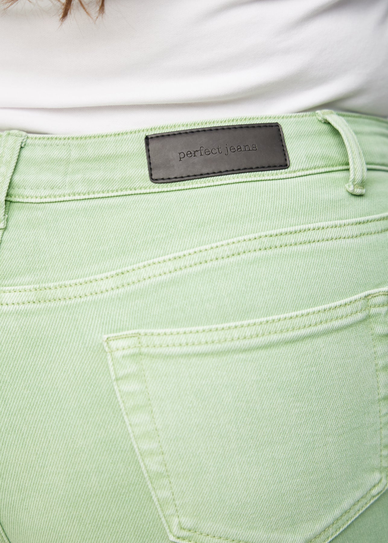 Nærbillede af lysegrønt jeansmateriale med Perfect Jeans læderpatch bagpå i taljen, på en plus-size model.
