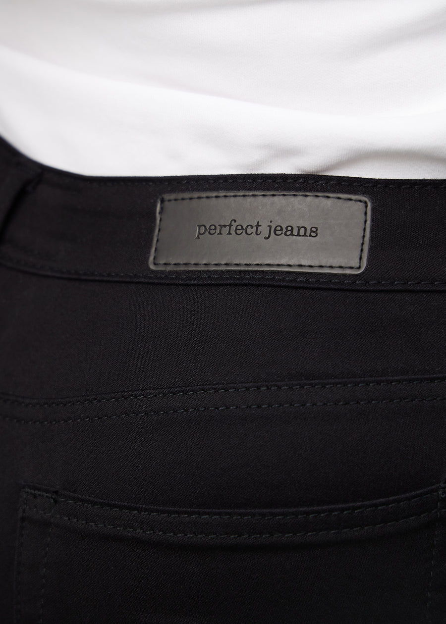 Nærbillede af sort jeansmateriale med Perfect Jeans læderpatch bagpå i taljen, på en plus-size model.