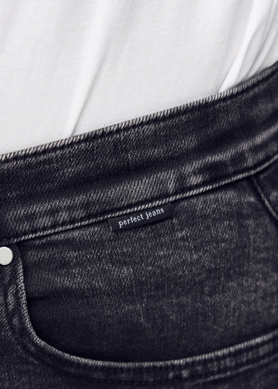 Nærbillede af mørkegrå denim med Perfect Jeans logoetiket ved forlommekanten.