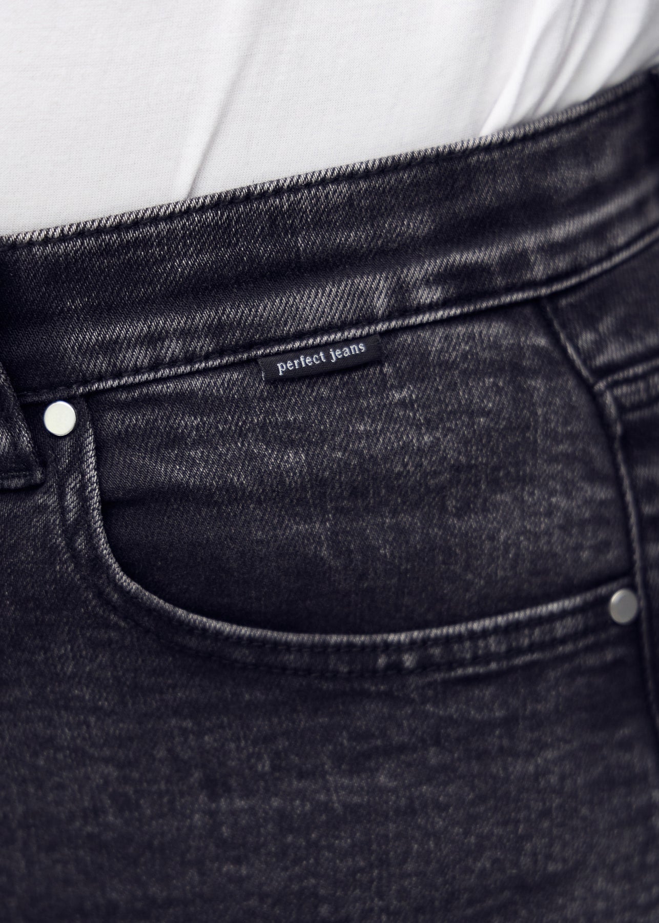 Nærbillede af mørkegrå denim med Perfect Jeans logoetiket ved forlommekanten, på en plus-size model.