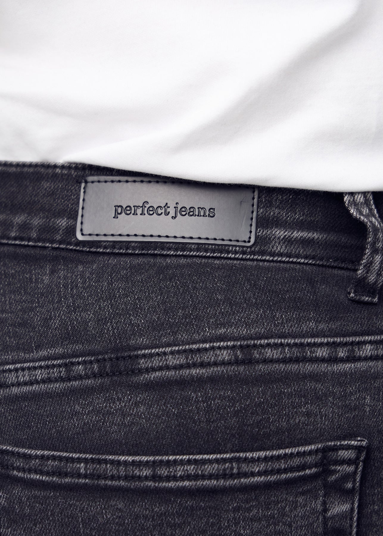 Nærbillede af mørkegrå denim med Perfect Jeans læderpatch bagpå i taljen, på en plus-size model.