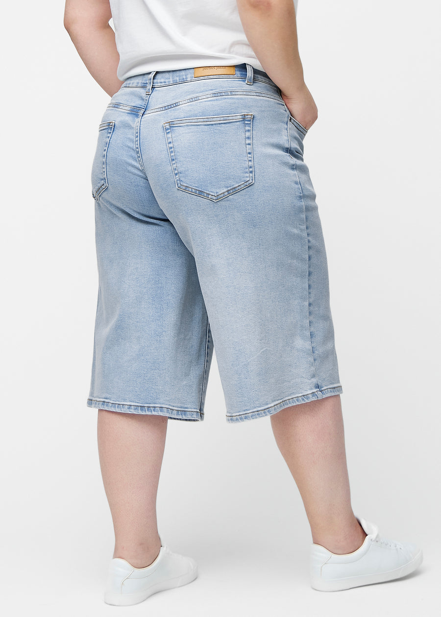 Lockere, hellblaue Denim-Capris in der Farbe Waves von hinten am Plus-Size-Model gesehen, sodass Passform und Länge sichtbar sind.