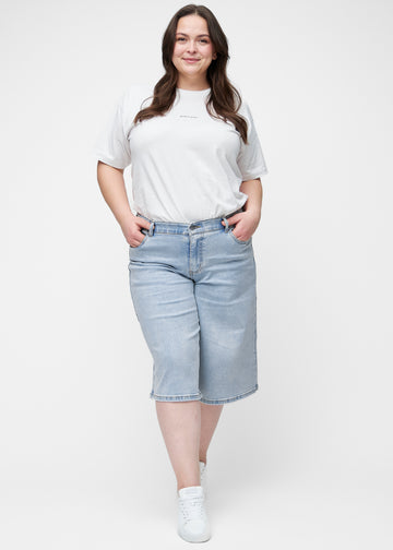 Ganzkörperbild des Plus-Size-Models in lockeren, hellblauen Denim-Capris in der Farbe Waves, die bis knapp unter das Knie reichen.