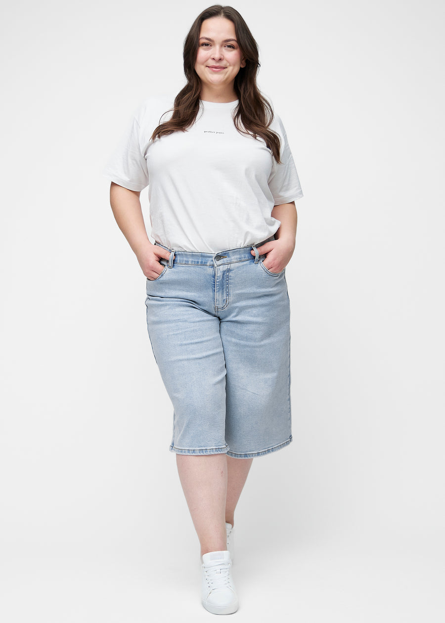 Ganzkörperbild des Plus-Size-Models in lockeren, hellblauen Denim-Capris in der Farbe Waves, die bis knapp unter das Knie reichen.