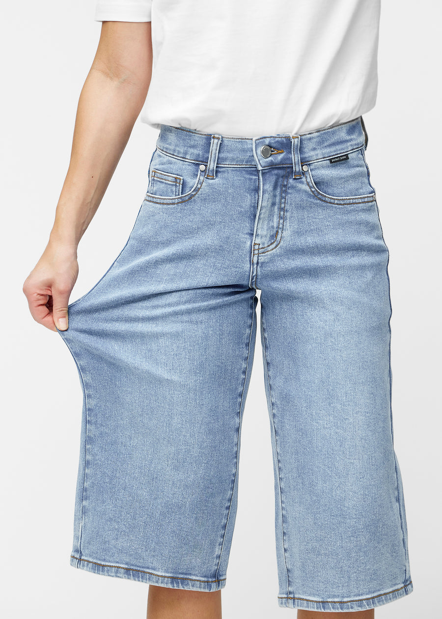 Model dehnt die lockeren, hellblauen Denim-Capris in der Farbe Waves an der Hüfte, um den Stretch des Materials zu zeigen.