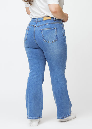 Blaue Mid-Rise-Bootcut-Jeans in der Farbe Rivers. Rückansicht an einem Plus-Size-Model, die gesamte Passform ist zu sehen.