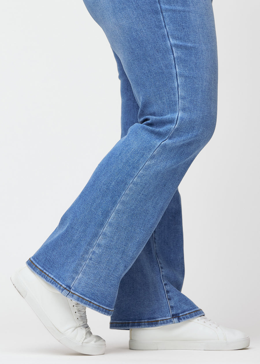 Blaue Mid-Rise-Bootcut-Jeans in der Farbe Rivers. Nahaufnahme am Knöchel eines Plus-Size-Model, um den leichten Schlag am Beinabschluss zu zeigen.
