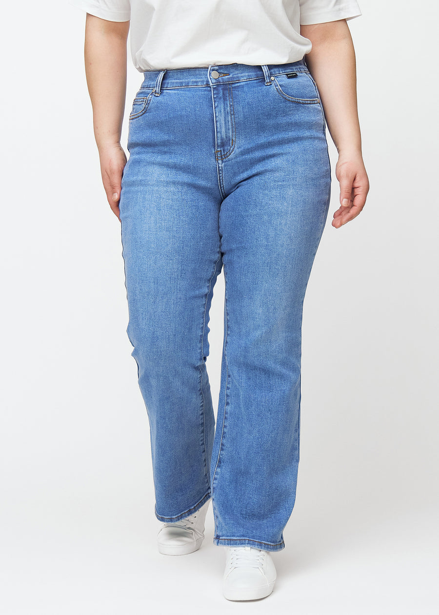 Blaue Mid-Rise-Bootcut-Jeans in der Farbe Rivers. Vorderansicht an einem Plus-Size-Model, an Hüfte und Oberschenkeln anliegend mit leicht ausgestelltem Bein.