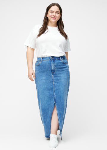 Fuldt billede af plus-size model i lang, klassisk blå denimnederdel i farven Rivers med regulær pasform og slids foran.