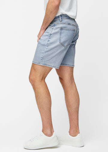 Model dehnt hellblaue Denim-Shorts für Herren in der Farbe Waves am Oberschenkel, um den Stretch des Materials zu zeigen.