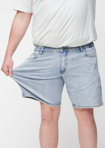 Plus-Size-Model dehnt hellblaue Denim-Shorts für Herren in der Farbe Waves am Oberschenkel, um den Stretch des Materials zu zeigen.