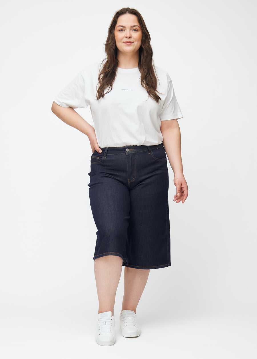 Ganzkörperbild eines Plus-Size-Models in tief dunkelblauen Denim-Capris für Damen in der Farbe Midnights mit Loose-Passform.