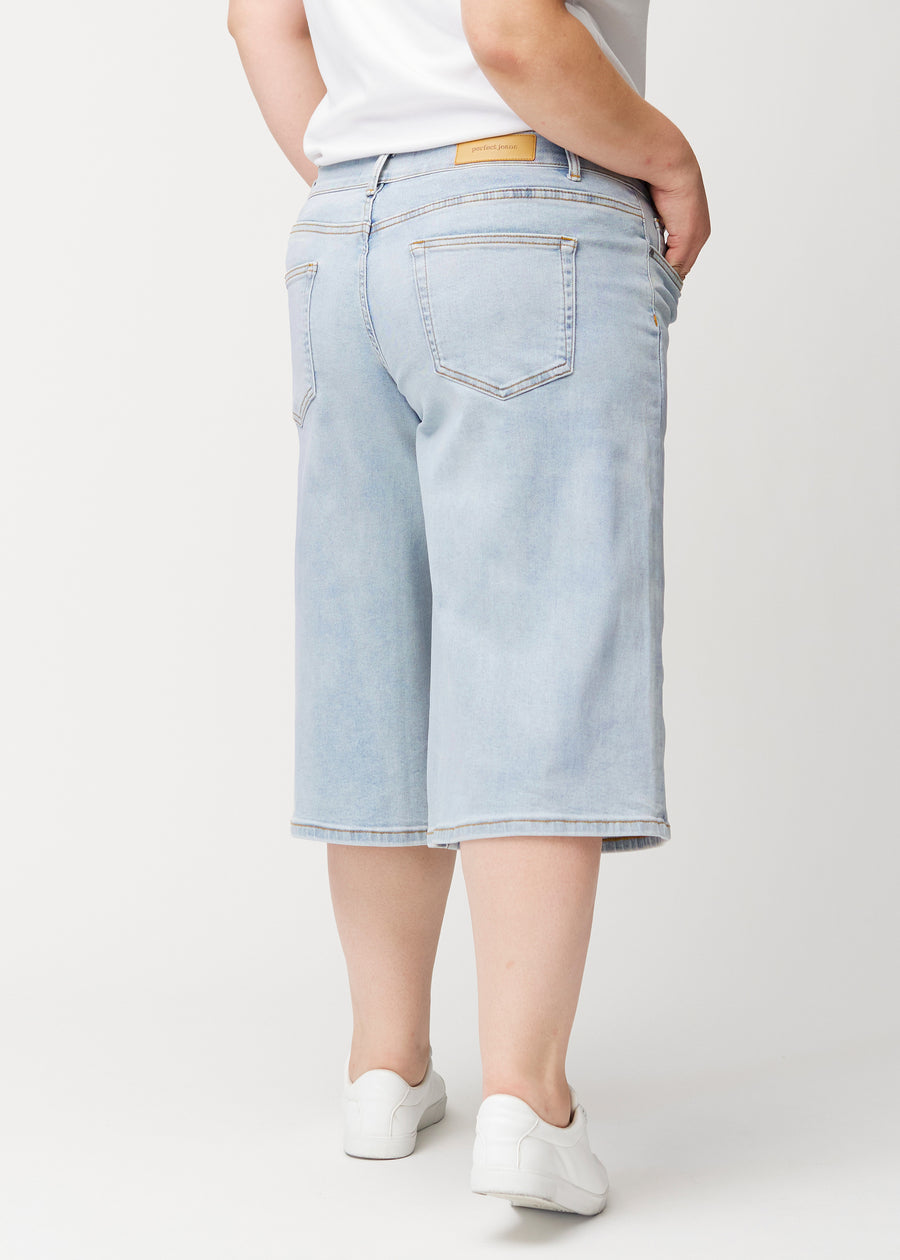 Rückansicht eines Plus-Size-Models in lockeren, hellblauen Waves Denim-Capris, die Passform und Länge zeigt.