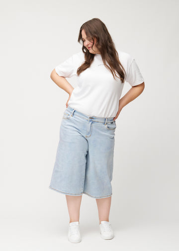 Ganzkörperaufnahme eines Plus-Size-Models in lockeren, hellblauen Waves Denim-Capris, die bis knapp unter das Knie reichen.