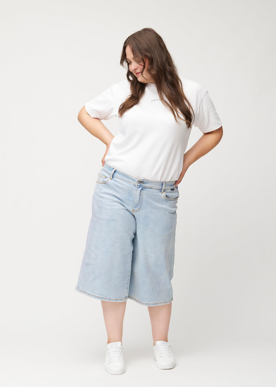 Ganzkörperaufnahme eines Plus-Size-Models in lockeren, hellblauen Waves Denim-Capris, die bis knapp unter das Knie reichen.