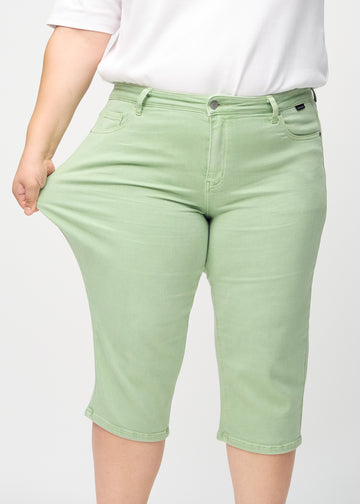Ein Plus-Size-Model zieht die Capris am Oberschenkel, um den Stretch zu zeigen.