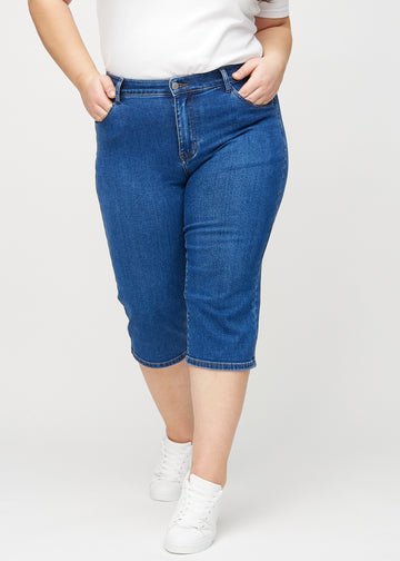 Dunkelblaue Denim-regular-Capris, Modellname Oceans, die an einer Plus-Size-Model am Bein gerade sitzen und knapp unter dem Knie enden, von vorn gesehen.