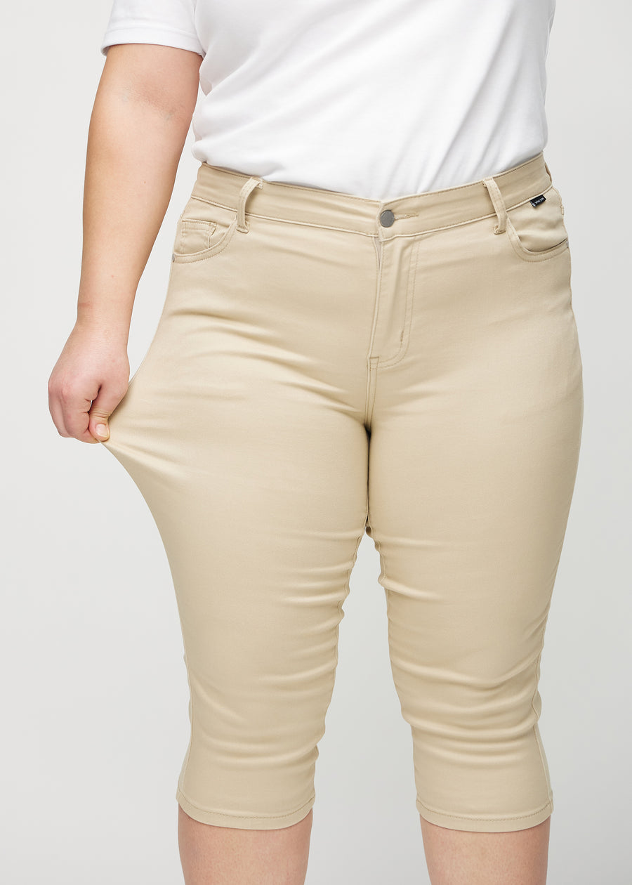 Skinny-Capris für Damen in beigefarbenem Jeansstoff, Farbe Gazelles. Ein Plus-Size-Model dehnt den Stoff, um den Stretch zu zeigen.