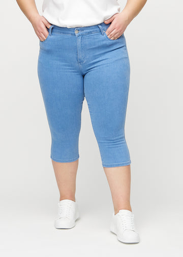 Skinny-Capris für Damen in blauem Jeansstoff, Farbe Geraniums. Vorderansicht an einem Plus-Size-Model, eng geschnitten bis knapp unter das Knie.