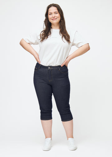 Ganzkörperbild eines Plus-Size-Models in tief dunkelblauen Denim-Capris für Damen in der Farbe Midnights mit Skinny-Passform.