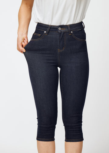 Model dehnt tief dunkelblaue Denim-Capris für Damen in der Farbe Midnights am Oberschenkel, um den Stretch des Materials zu zeigen.