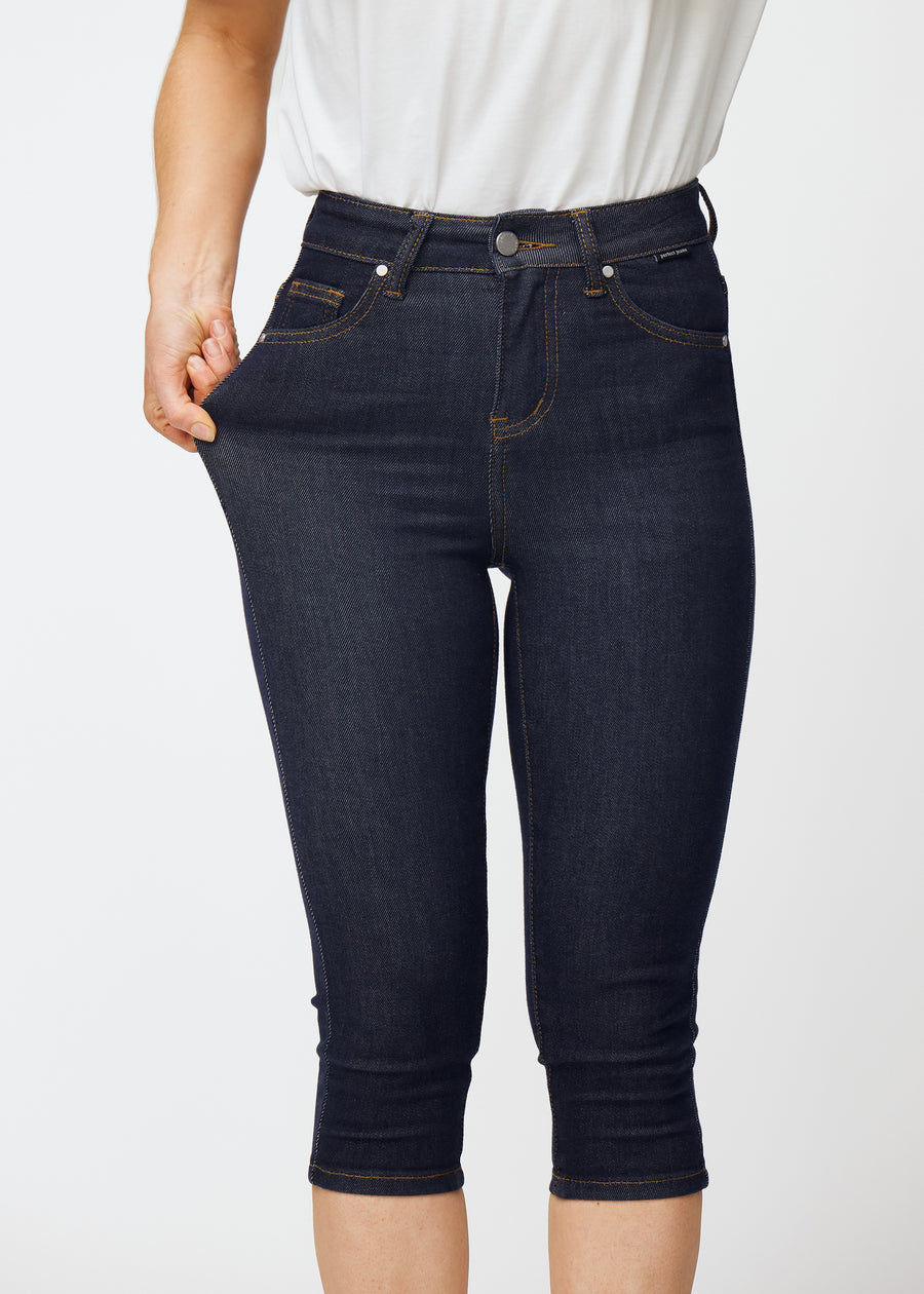 Model dehnt tief dunkelblaue Denim-Capris für Damen in der Farbe Midnights am Oberschenkel, um den Stretch des Materials zu zeigen.