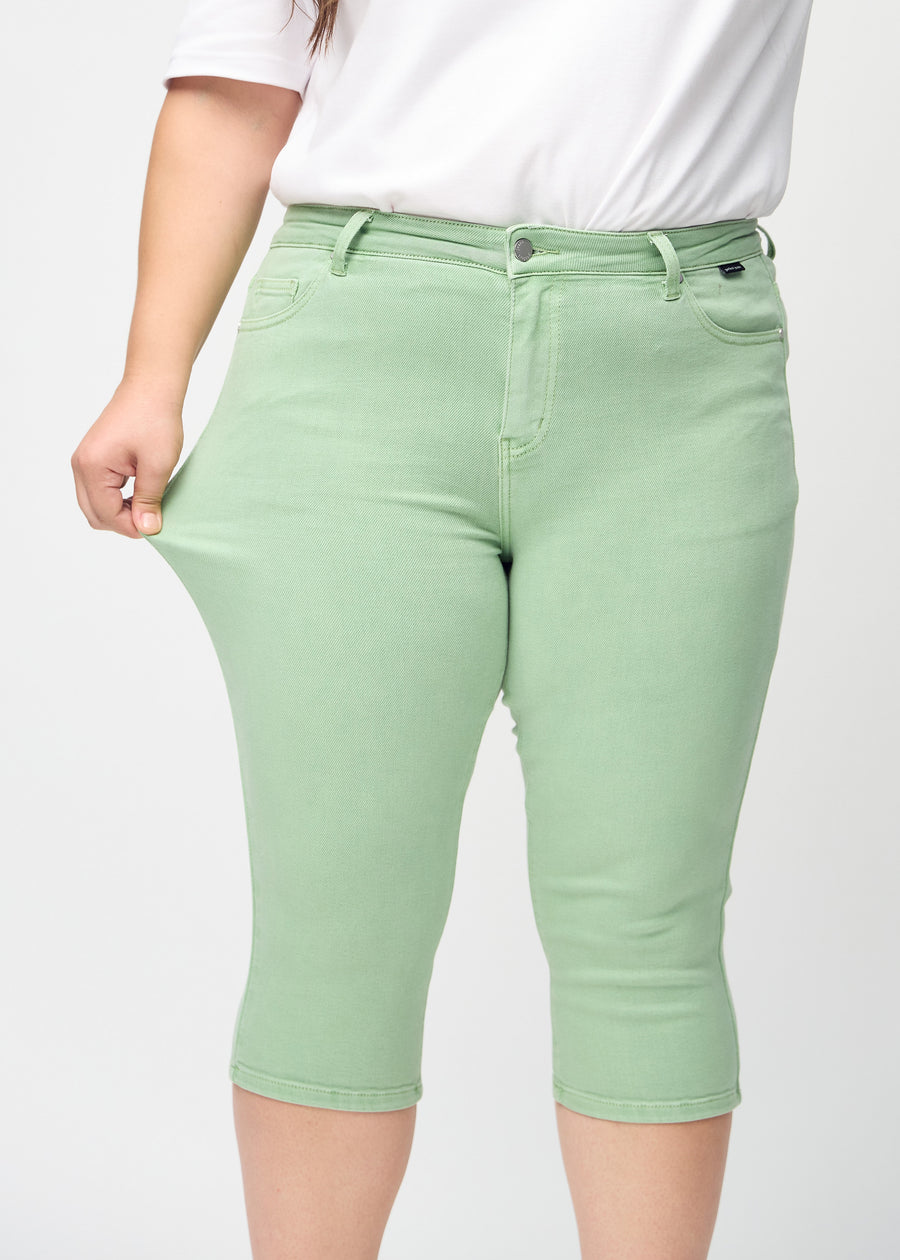 Skinny-Capris für Damen in pastellgrünem Jeansstoff, Farbe Mints. Ein Plus-Size-Model dehnt den Stoff, um den Stretch zu zeigen.