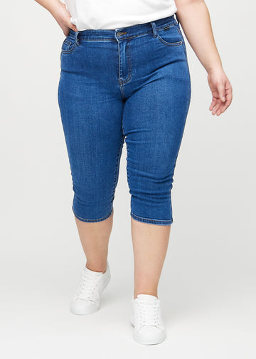 Skinny-Capris für Damen in dunkelblauem Denim, Farbe Oceans. Vorderansicht an einem Plus-Size-Model, eng geschnitten bis knapp unter das Knie.