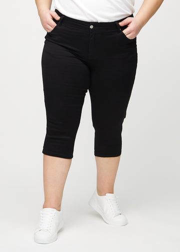 Skinny-Capris für Damen in schwarzem Jeansstoff, Farbe Ravens. Vorderansicht an einem Plus-Size-Model, eng geschnitten bis knapp unter das Knie.