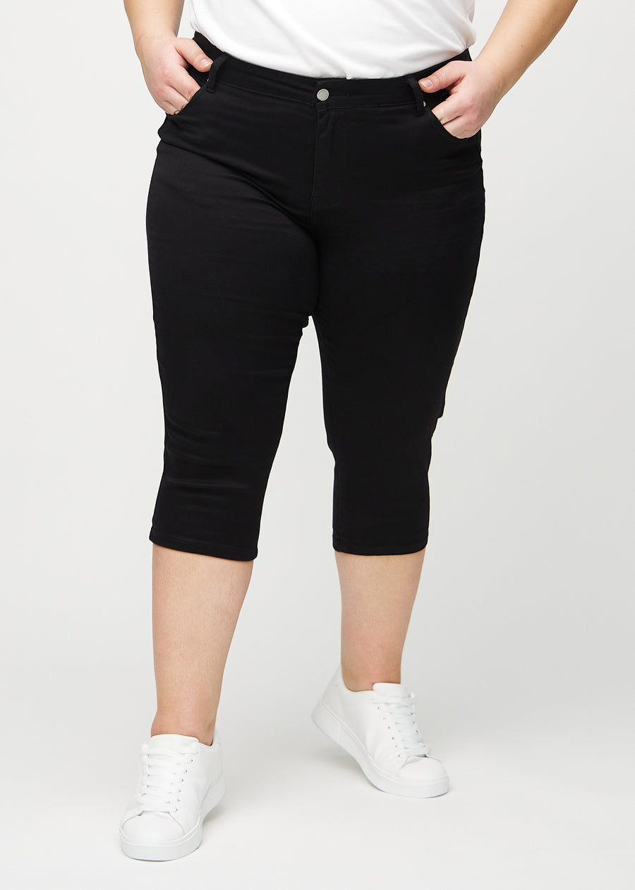 Skinny-Capris für Damen in schwarzem Jeansstoff, Farbe Ravens. Vorderansicht an einem Plus-Size-Model, eng geschnitten bis knapp unter das Knie.
