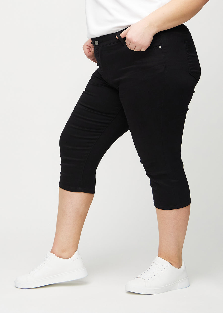 Skinny-Capris für Damen in schwarzem Jeansstoff, Farbe Ravens. Seitenansicht an einem Plus-Size-Model, die figurbetonte Passform ist zu sehen.