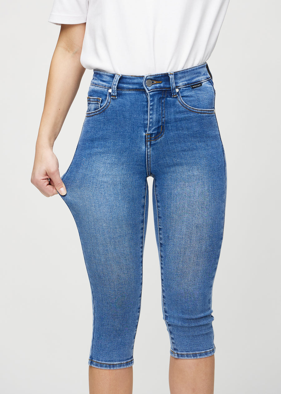 Skinny-Capris für Damen in blauem Denim, Farbe Rivers. Ein Model dehnt den Stoff, um den Stretch zu zeigen.