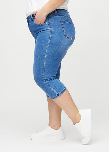 Skinny-Capris für Damen in blauem Denim, Farbe Rivers. Seitenansicht an einem Plus-Size-Model, die figurbetonte Passform ist zu sehen.