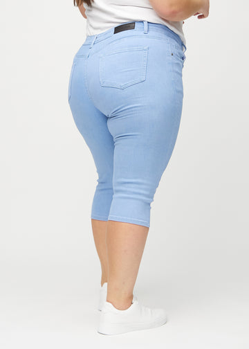Skinny-Capris für Damen in hellblauem Jeansstoff, Farbe Skies. Rückansicht an einem Plus-Size-Model, zeigt die Passform und Gesäßtaschen.