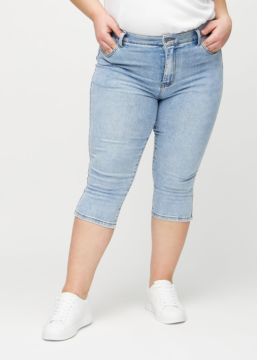 Hellblaue Denim-skinny-Capris, Modellname Waves, die eng am Bein anliegen und direkt unter dem Knie enden, an einem Plus-Size-Model von vorn gesehen.