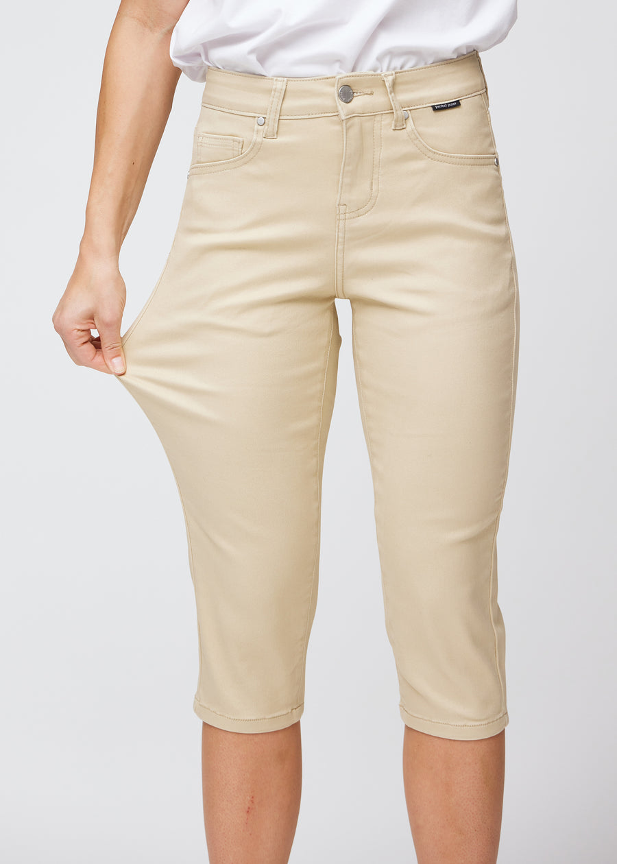Slim-Capris für Damen aus beigefarbenem Jeansstoff, Farbe Gazelles. Ein Model dehnt den Stoff am Oberschenkel, um die Flexibilität zu zeigen.