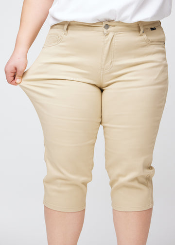 Slim-Capris für Damen aus beigefarbenem Jeansstoff, Farbe Gazelles. Ein Plus-Size-Model dehnt den Stoff am Oberschenkel, um die Flexibilität zu zeigen.