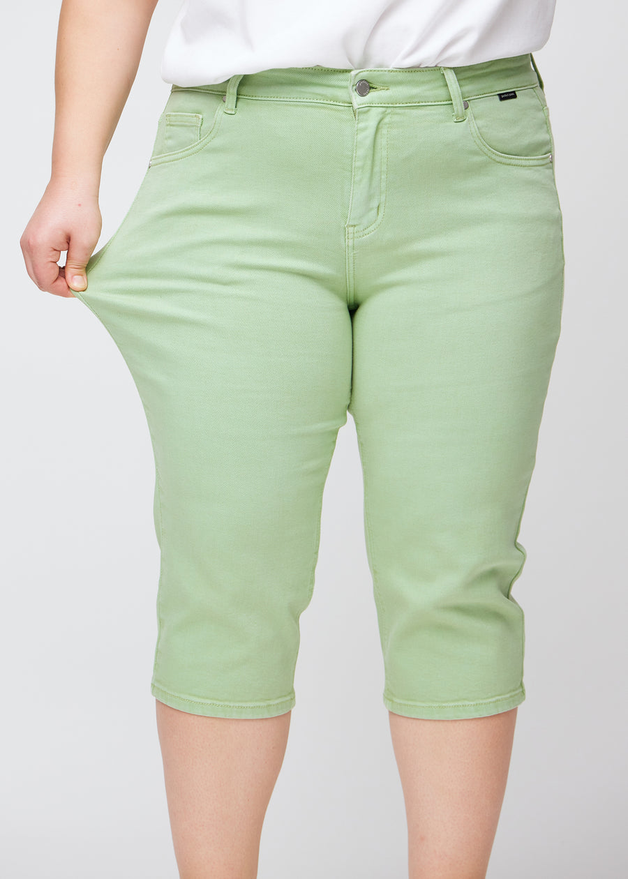 Slim-Capris für Damen aus pastellhellgrünem Jeansstoff, Farbe Mints. Ein Plus-Size-Model dehnt den Stoff am Oberschenkel, um die Flexibilität zu zeigen.