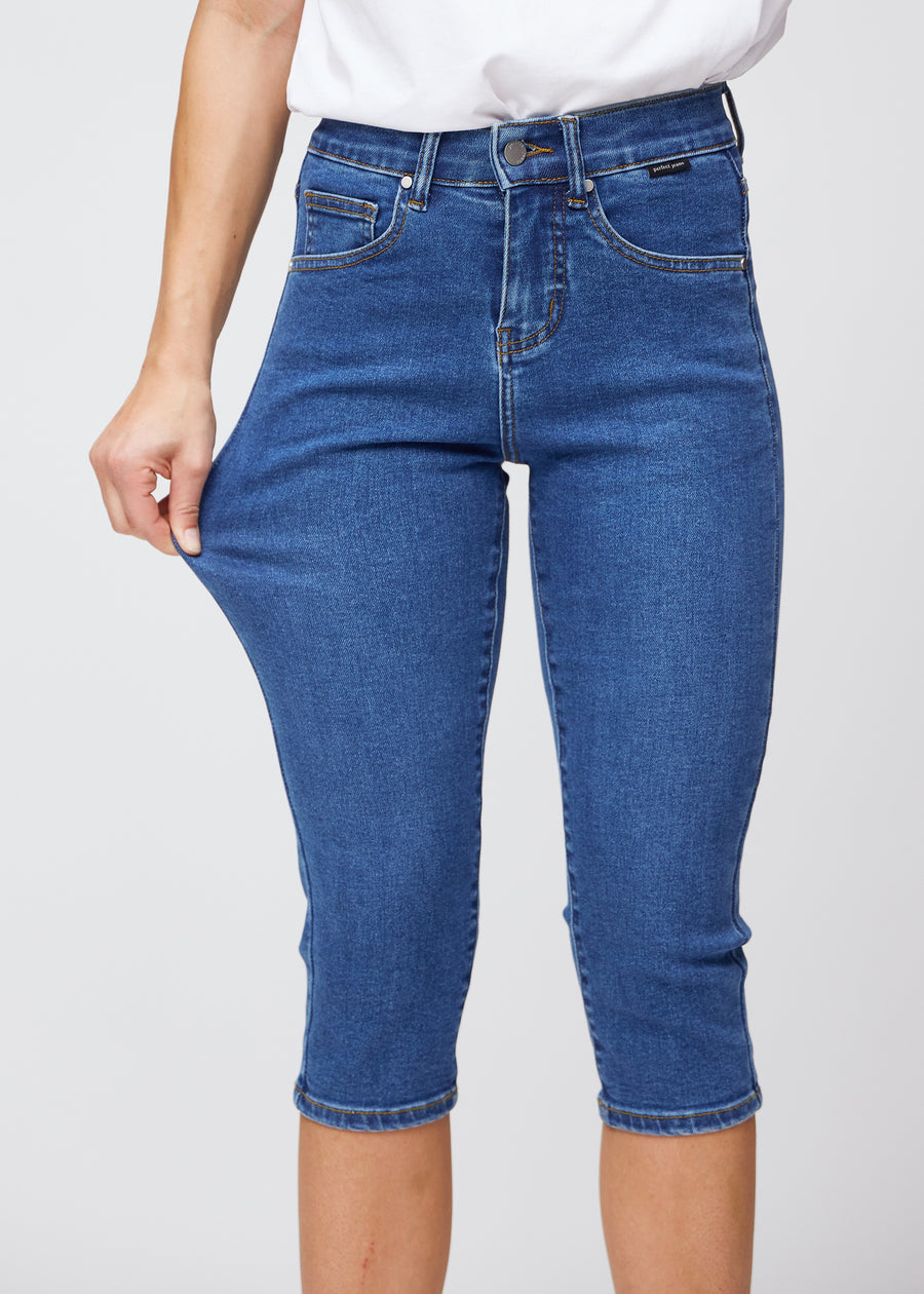 Das Model zieht die Capris am Oberschenkel, um den weichen und flexiblen Stretch im dunkelblauen Denim zu zeigen.