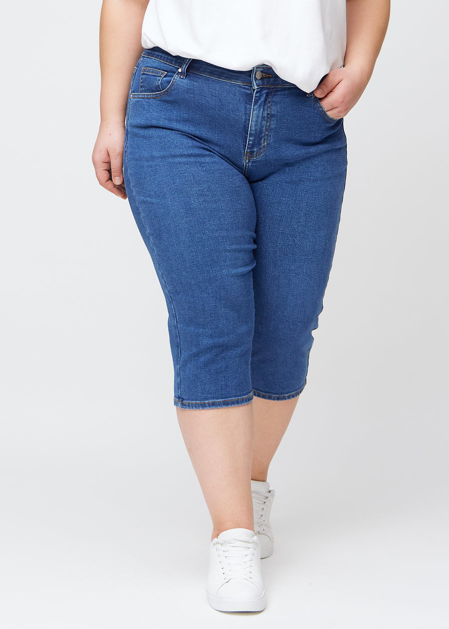 Dunkelblaue Denim-slim-Capris, Farbe Oceans, mit enger Passform und Länge direkt unter dem Knie, von vorne an einem Plus-Size-Model gesehen.