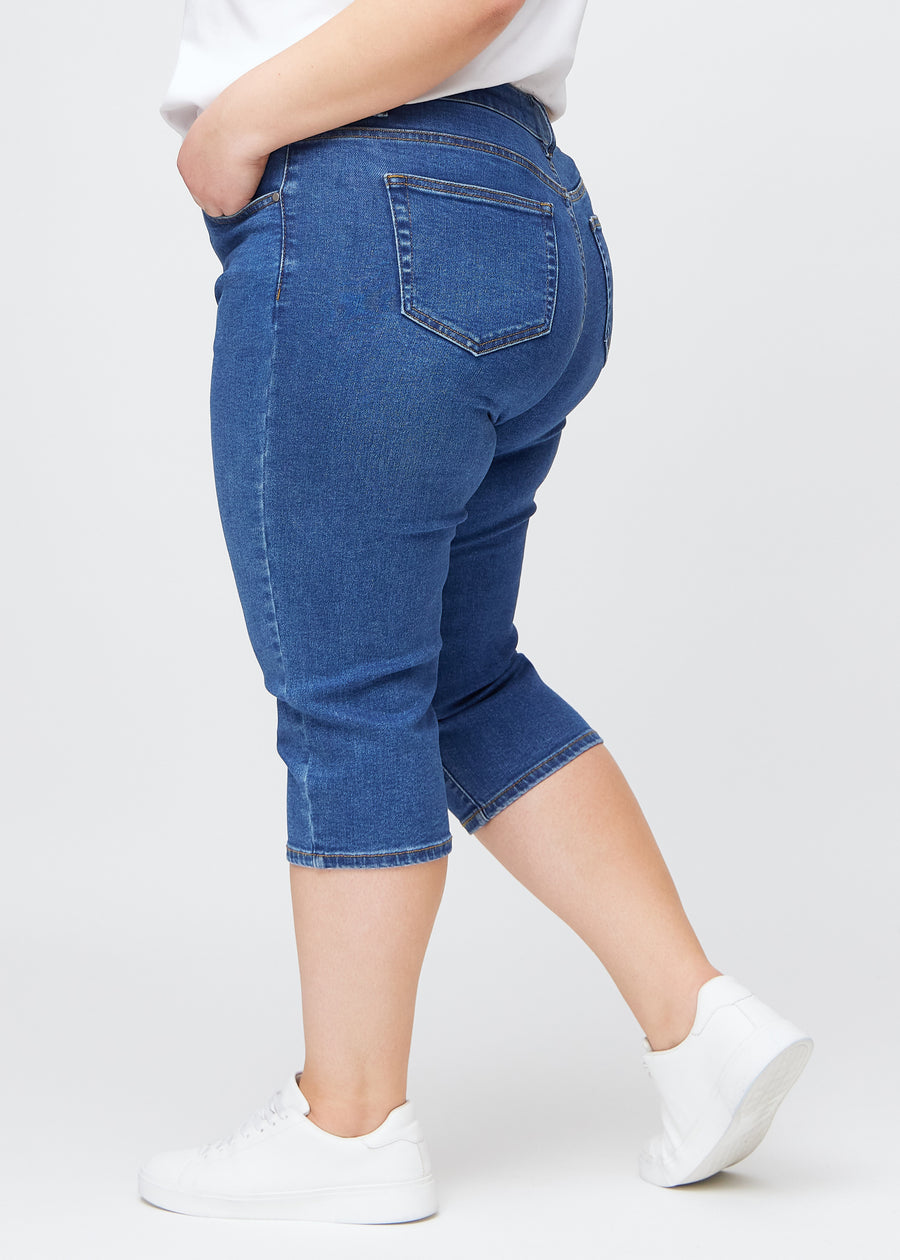 Dunkelblaue Denim-slim-Capris in der Farbe Oceans, von der Seite an einem Plus-Size-Model gesehen, sodass Passform und Silhouette sichtbar sind.