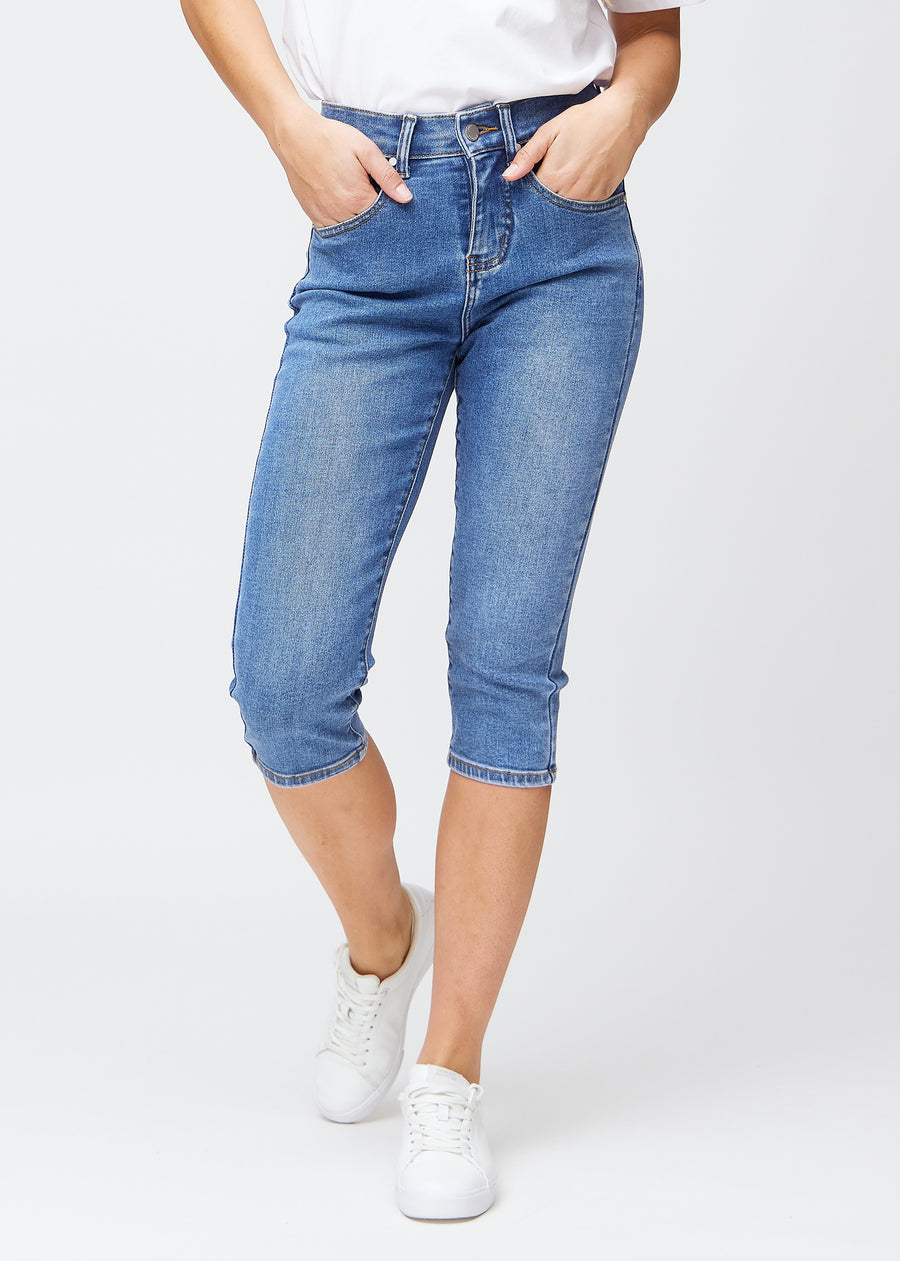 Slim-Capris für Damen aus blauem Denim, Farbe Rivers. Vorderansicht an einem Model, figurbetonter Schnitt bis knapp unter das Knie.