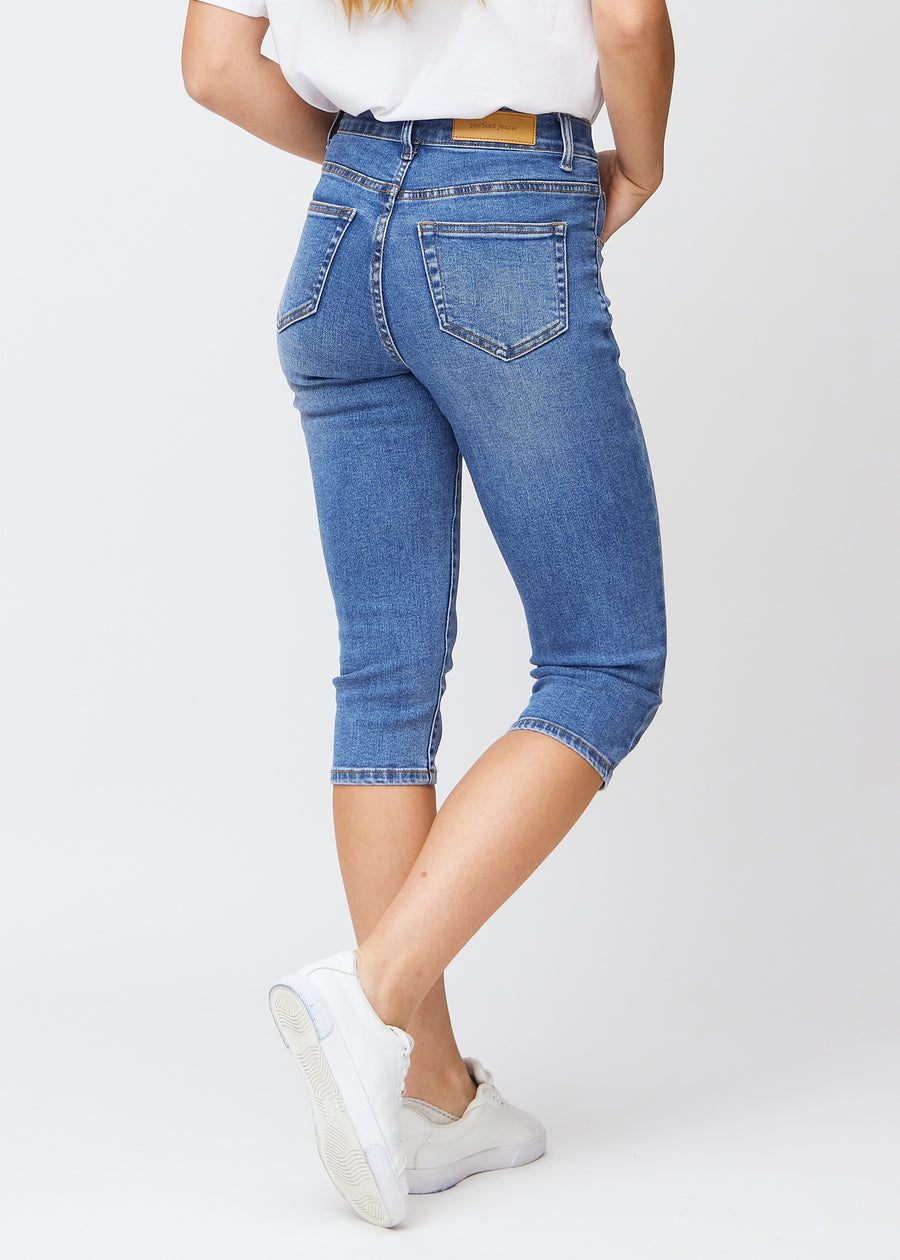 Slim-Capris für Damen aus blauem Denim, Farbe Rivers. Rückansicht an einem Model, zeigt Passform, Länge und Gesäßtaschen.