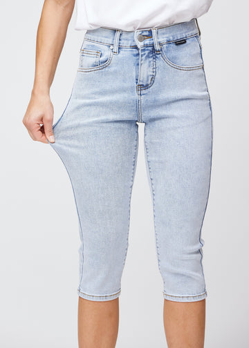 Slim-Capris für Damen aus hellblauem Denim, Farbe Waves. Ein Model dehnt den Stoff am Oberschenkel, um die Flexibilität zu zeigen.