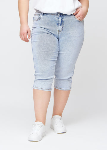 Slim-Capris für Damen aus hellblauem Denim, Farbe Waves. Vorderansicht an einem Plus-Size-Model, figurbetonter Schnitt bis knapp unter das Knie.